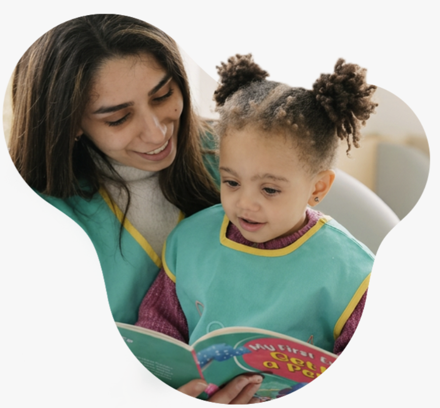 A caregiver reading a picture book with a toddler at Poupon City